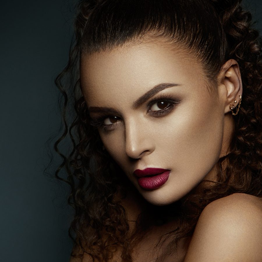 Beautiful face of a fashion model with black eyes.Curly hair. Pink lips. Studio portrait.